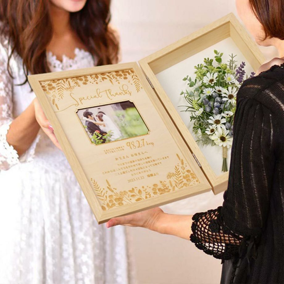 木製ボードにメッセージがレーザー刻印されたブーケ付き子育て感謝状を母に贈呈している花嫁